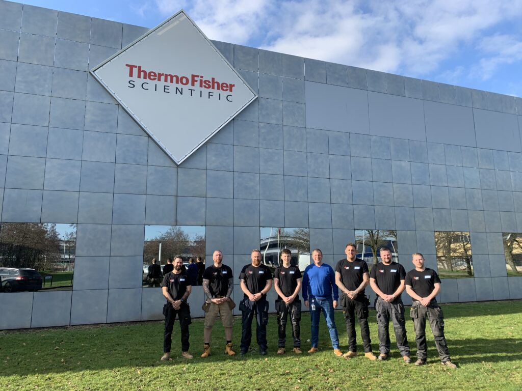 Our team standing outside an industrial building, posing for a photograph underneath a sign that says Thermo Fisher Scientific